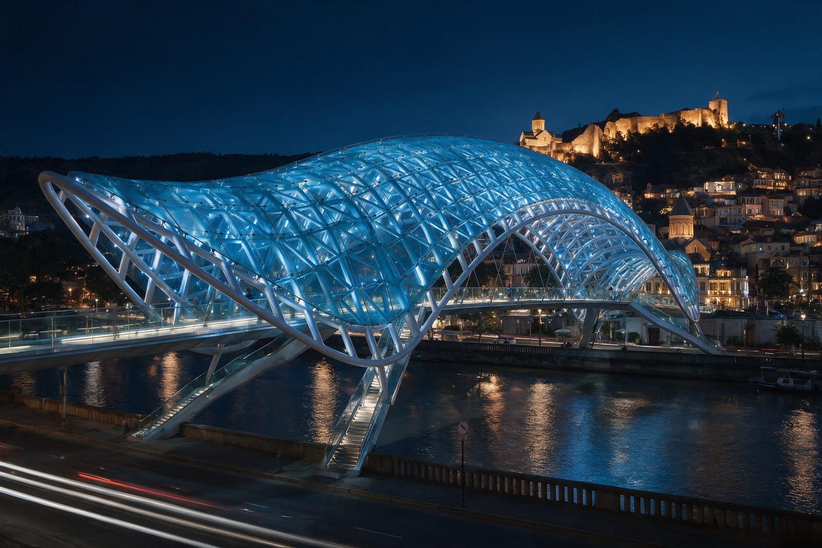 Tiflis’te geceleri aydınlatılmış modern köprü ve eski şehir